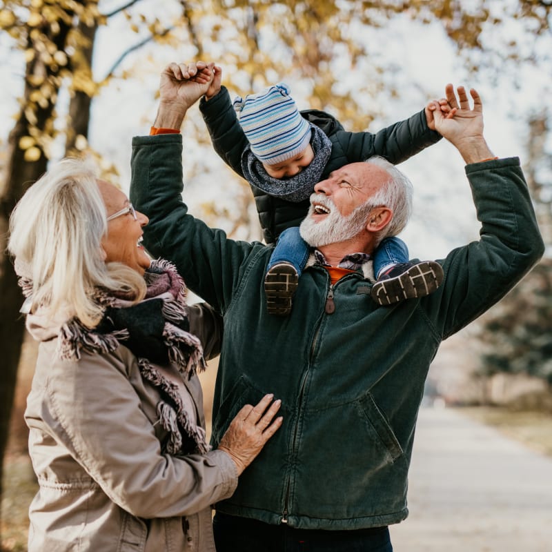 An older couple are on a trail and the man has his grandchild sitting on his shoulders.