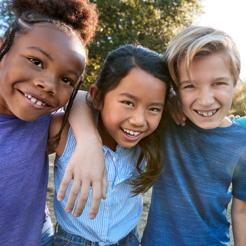 Three kids smile and have their arms around each other.