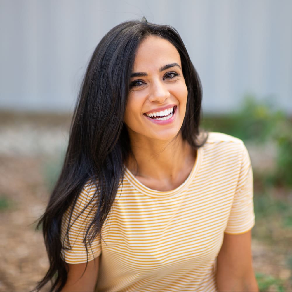 A woman with long brown hair and a yellow shirt is smiling at the camera.