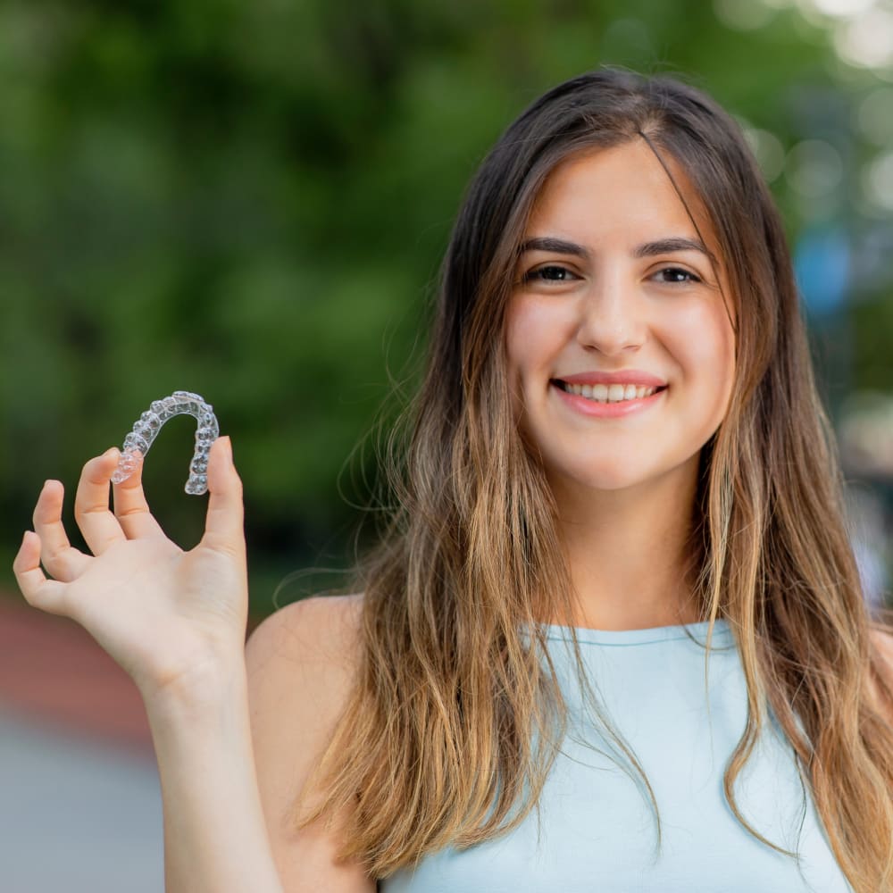 A young woman holds up an Invisalign clear aligner tray.