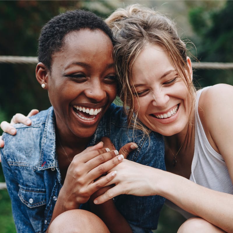 Two women are laughing with their arms around each other.