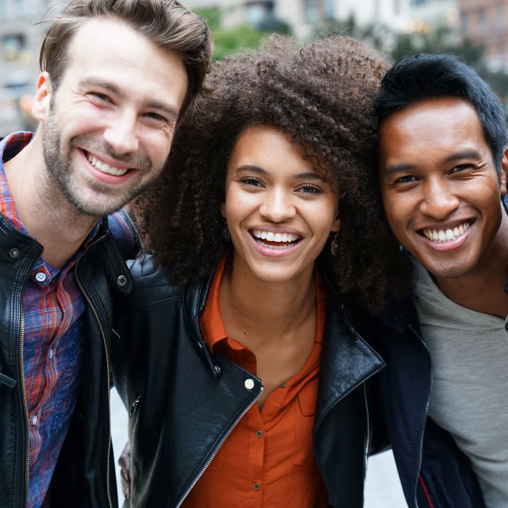 A group of three people smile with their arms around each other.